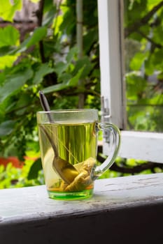 Tea and tea bag under the summer sun. A tea bag in a glass transparent mug on the old windowsill village and against the background of green summer trees.