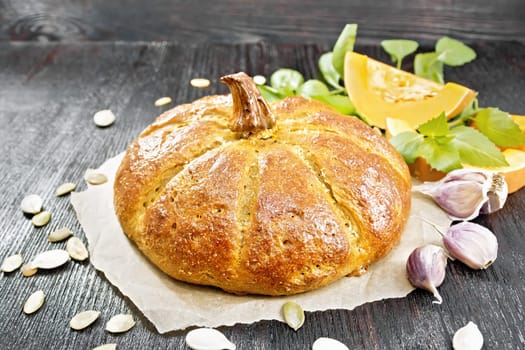 Pumpkin bread on parchment, garlic, basil, pieces and seeds of a vegetable on the background of a dark wooden board