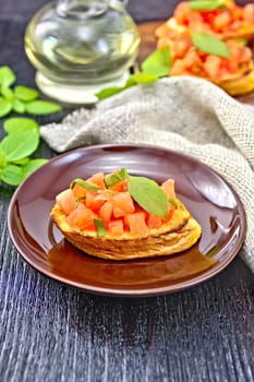 Bruschetta with tomatoes and basil in a plate, napkin and vegetable oil in a decanter on wooden board background