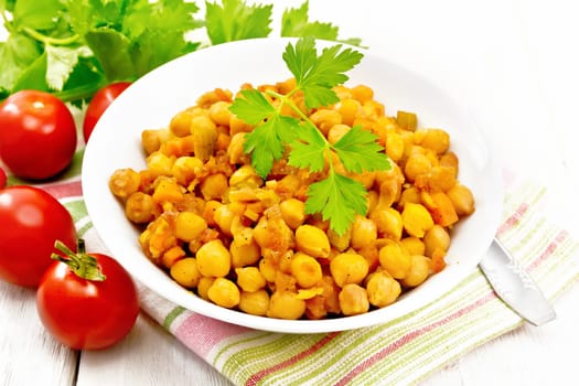 Stewed chickpeas with celery, tomatoes, onions, carrots and garlic in a plate on a napkin on wooden board background