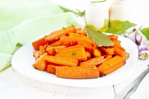 Carrots fried with garlic, bay leaf, spices and green onions in a plate, basil and a napkin on light wooden board background