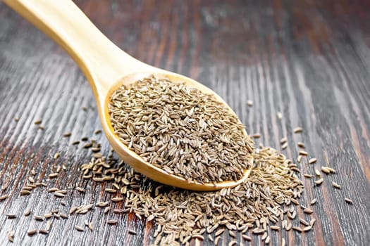 Cumin seeds in a spoon on a brown wooden board background