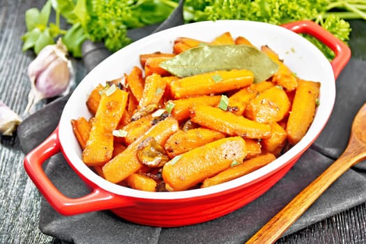 Carrots fried with garlic, bay leaf, spices and green onions in a pan on a napkin, basil and parsley on wooden board background