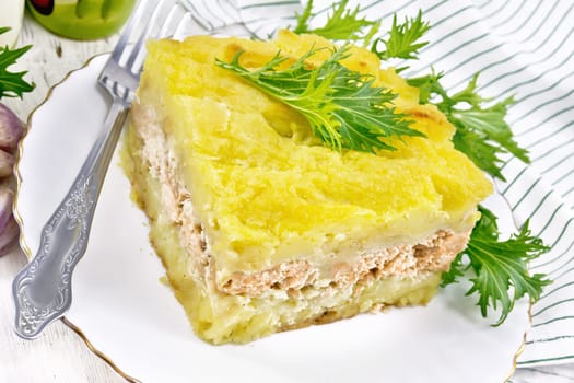 Mashed potato casserole with salmon fillet and lettuce in a plate, towel, garlic on the background of a light wooden board