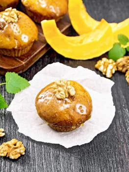 Small pumpkin cupcake with orange glaze and walnuts on paper, sprigs of mint on a dark wooden board background