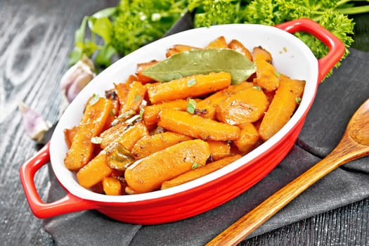 Carrots fried with garlic, bay leaf, spices and green onions in a pan on a napkin, basil and parsley on black wooden board background