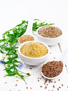 Linen bran and flour in two white bowls, seeds in spoons, flax leaves and flowers on the background of a wooden board