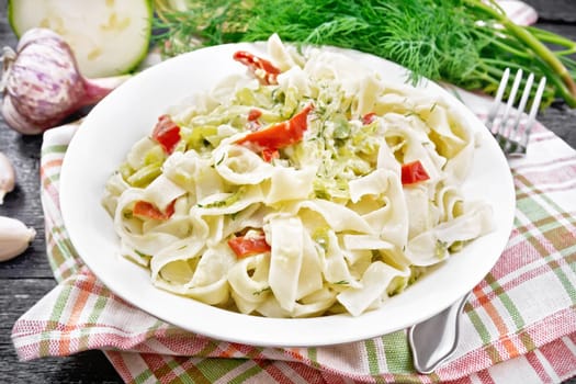 Fettuccine pasta with zucchini and hot red pepper in creamy sauce in white plate on a towel, garlic and a fork on black wooden board background