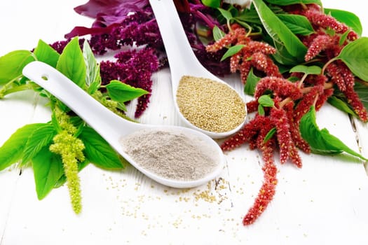 Flour and seeds amaranth in two spoons, multicolored flowers and leaves of a plant on wooden board background