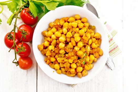 Chickpeas stewed with celery, tomatoes, onions, carrots and garlic in a plate on a towel on wooden board background from above