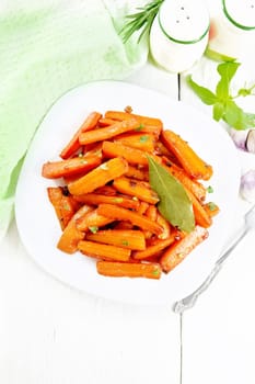 Carrots fried with garlic, bay leaf, spices and green onions in a plate, basil and napkin on wooden board background from above
