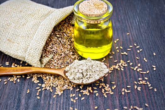 Flax flour in a spoon, oil in a glass jar, linen seeds in a bag on a dark wooden board background