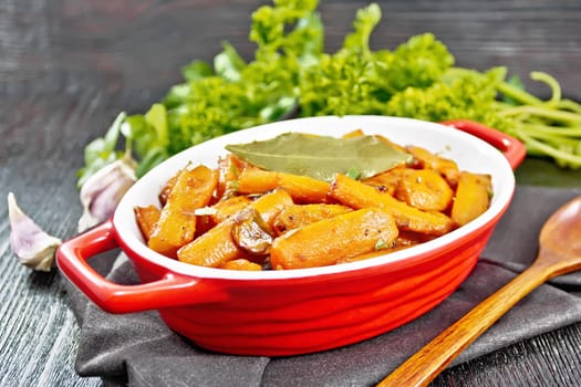 Carrots fried with garlic, bay leaf, spices and green onions in a pan on a napkin, basil and parsley on dark wooden board background
