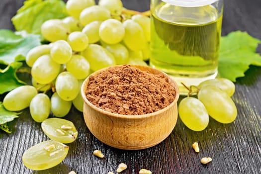 Grape seed flour in a bowl, oil in a jar and berries and grape seeds on wooden board background
