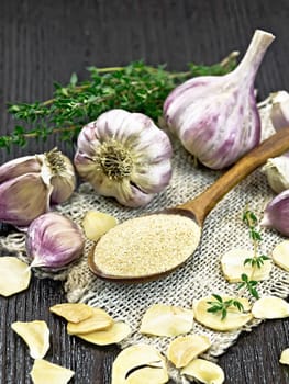 Ground garlic in a spoon on burlap, dried and fresh garlic, bunch of thyme on the background of wooden board