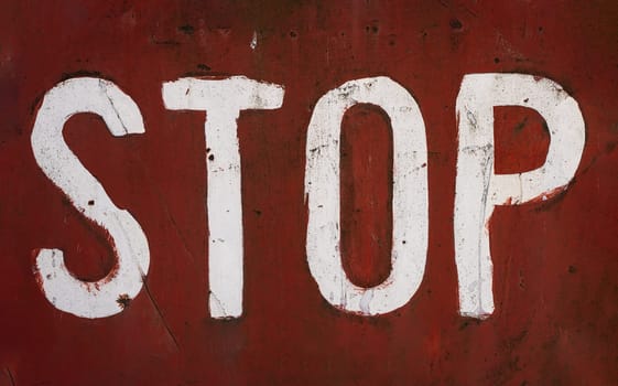 front view closeup of word stop written with white paint and capital letters brush typeface style on red rusted metallic plate texture