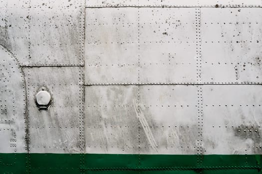 front view closeup of old airplane metallic hull fuselage plating with rows of bolts and rivets industrial texture