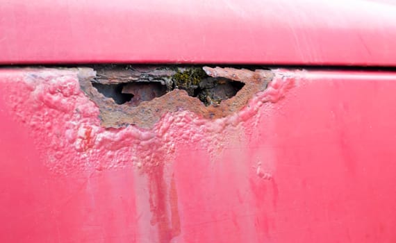 Rusty wing. Corrosion of the body of a red old car after winter. Influence of reagents in winter on an unprotected vehicle body. Left side damage