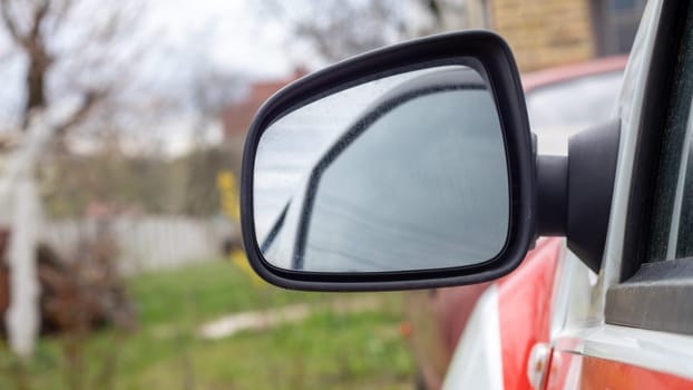 Side left black plastic rearview mirror on a white car. Exterior side-view mirror on the driver's side, electrically adjustable and heated