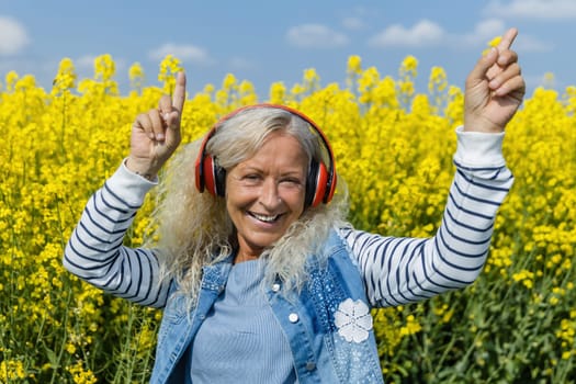 Elderly Woman listen to music with headphones in blooming canola field
