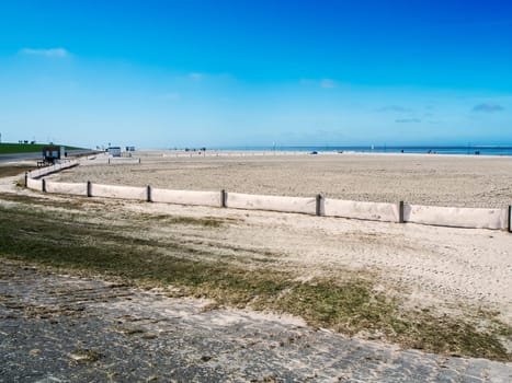 Landscape view of the smoothed bathing beach with fence near Neuharlingersiel in East Friesland in March 2022 with a blue sky and a view to the horizon.