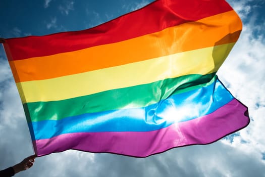 Bright rainbow LGBT flag fluttering against blue sky. LGBT community, happiness, freedom and love concept for same sex couples.