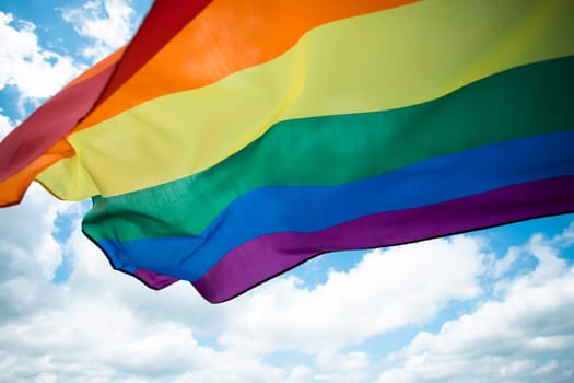 Bright rainbow LGBT flag fluttering against blue sky. LGBT community, happiness, freedom and love concept for same sex couples.