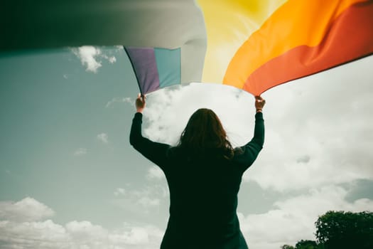 Woman sitting in a green meadow holding a Gay Rainbow Flag. Bisexual,gay, lesbian, transsexual symbol. Happiness, freedom and love concept for same sex couples