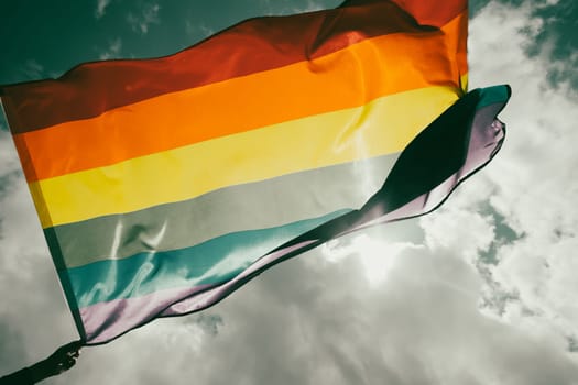 Bright rainbow LGBT flag fluttering against blue sky. LGBT community, happiness, freedom and love concept for same sex couples.
