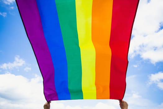 Bright rainbow LGBT flag fluttering against blue sky. LGBT community, happiness, freedom and love concept for same sex couples.