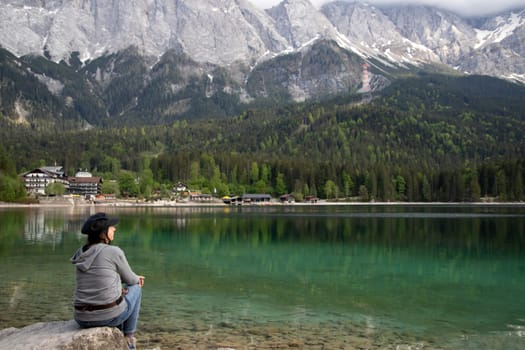 Tourist sitting on a rock and watching a beautiful view over lake Eibsee in the Bavarian Alps. Famous touristic destination in Europe