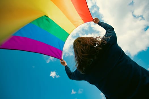 Woman sitting in a green meadow holding a Gay Rainbow Flag. Bisexual,gay, lesbian, transsexual symbol. Happiness, freedom and love concept for same sex couples