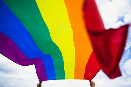 Bright rainbow LGBT flag fluttering against blue sky. LGBT community, happiness, freedom and love concept for same sex couples.