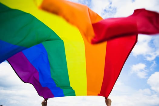 Bright rainbow LGBT flag fluttering against blue sky. LGBT community, happiness, freedom and love concept for same sex couples.