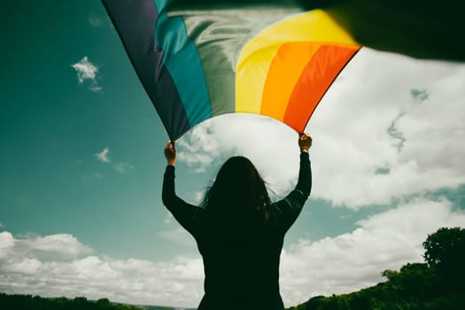 Woman sitting in a green meadow holding a Gay Rainbow Flag. Bisexual,gay, lesbian, transsexual symbol. Happiness, freedom and love concept for same sex couples