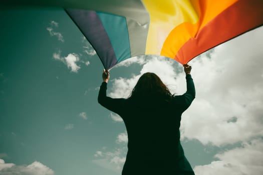 Woman sitting in a green meadow holding a Gay Rainbow Flag. Bisexual,gay, lesbian, transsexual symbol. Happiness, freedom and love concept for same sex couples