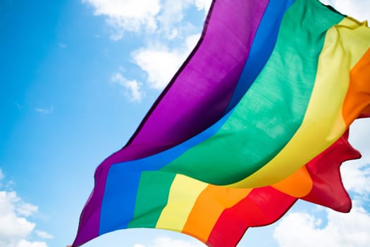 Bright rainbow LGBT flag fluttering against blue sky. LGBT community, happiness, freedom and love concept for same sex couples.