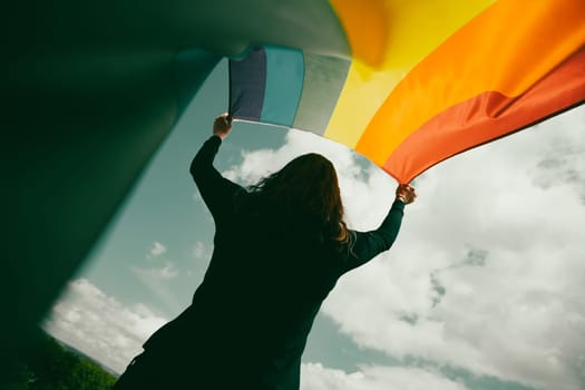 Woman sitting in a green meadow holding a Gay Rainbow Flag. Bisexual,gay, lesbian, transsexual symbol. Happiness, freedom and love concept for same sex couples