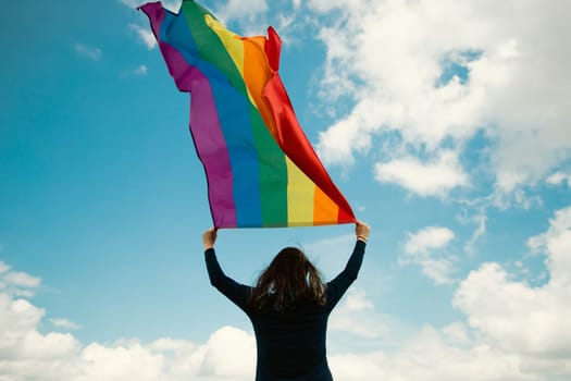 Woman sitting in a green meadow holding a Gay Rainbow Flag. Bisexual,gay, lesbian, transsexual symbol. Happiness, freedom and love concept for same sex couples