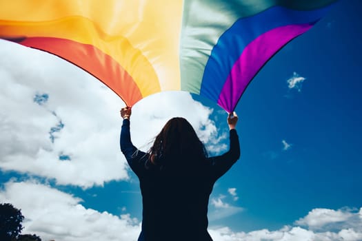 Woman sitting in a green meadow holding a Gay Rainbow Flag. Bisexual,gay, lesbian, transsexual symbol. Happiness, freedom and love concept for same sex couples