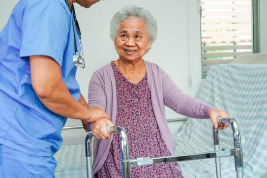 Doctor help Asian elderly woman disability patient walk with walker in nursing hospital, medical concept.