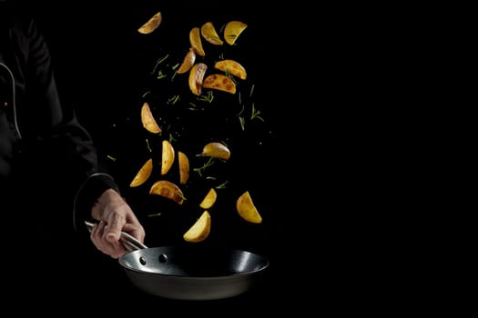 Crop faceless male chef in uniform tossing delicious cut potatoes and herbs in frying pan while preparing appetizing dinner against black background
