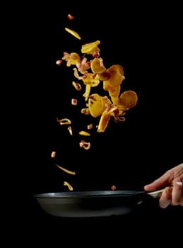 Crop unrecognizable male chef holding frying pan and tossing sliced potatoes and bacon while preparing delicious dinner against black background
