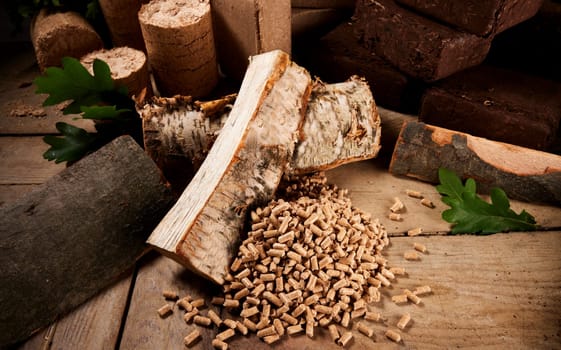 High angle of chopped birch and oak firewood scattered on wooden table near fuel pellets and cylindrical and square biomass briquettes