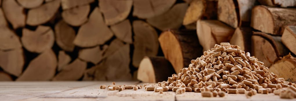 Ground level of pile of wood compressed fuel pellets stacked on floor near heap of firewood in sunlight