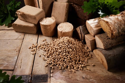 From above of set of various firewood and biofuel briquettes arranged on aged wooden table with stack of pellets