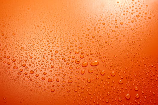 Full frame of wet clear orange background with condense and clear small round water drops flowing down in light room