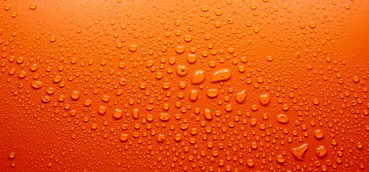 Panoramic view full frame of abstract clean orange background covered with various transparent round drops of water in light room