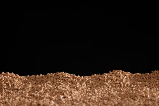 Heap of small beige biofuel pellets stacked in black studio as abstract background