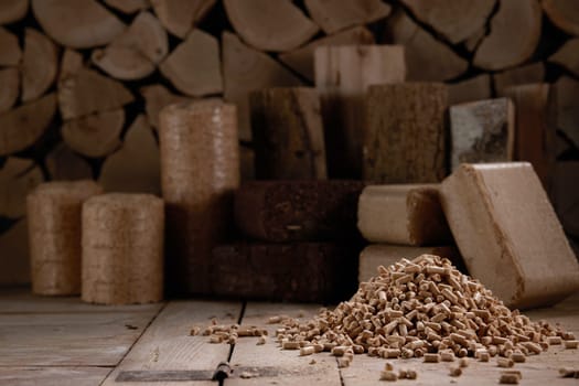 Set of various biomass briquettes made of compressed peat and placed near stack of firewood and scattered fuel pellets